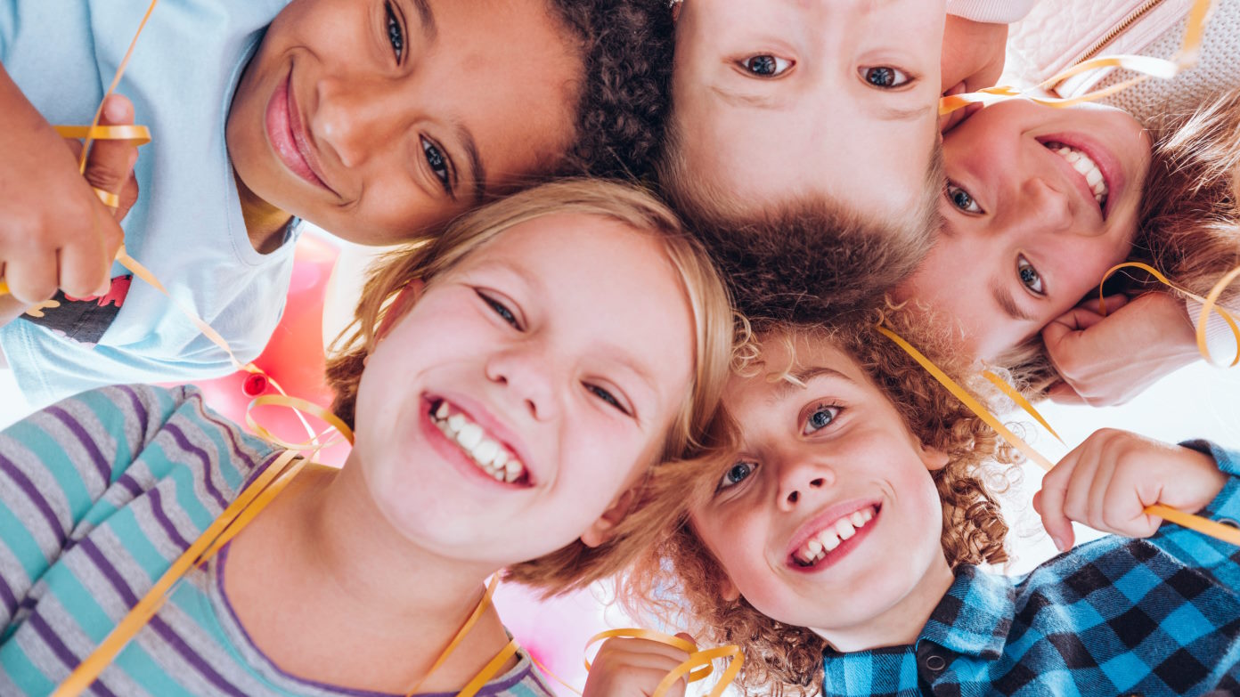 Fünf Kinder die Ihre Köpfe lächelnd in die Kamera strecken.